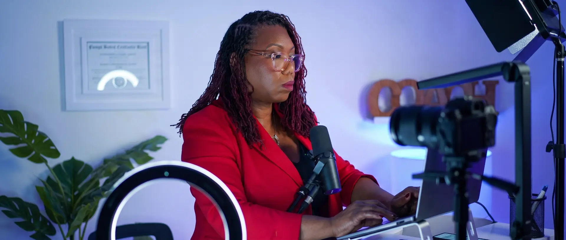 Coach Key, LaKeysha Cobbs-Hayes, recording an episode at her desk in a red blazer, microphone in frame.