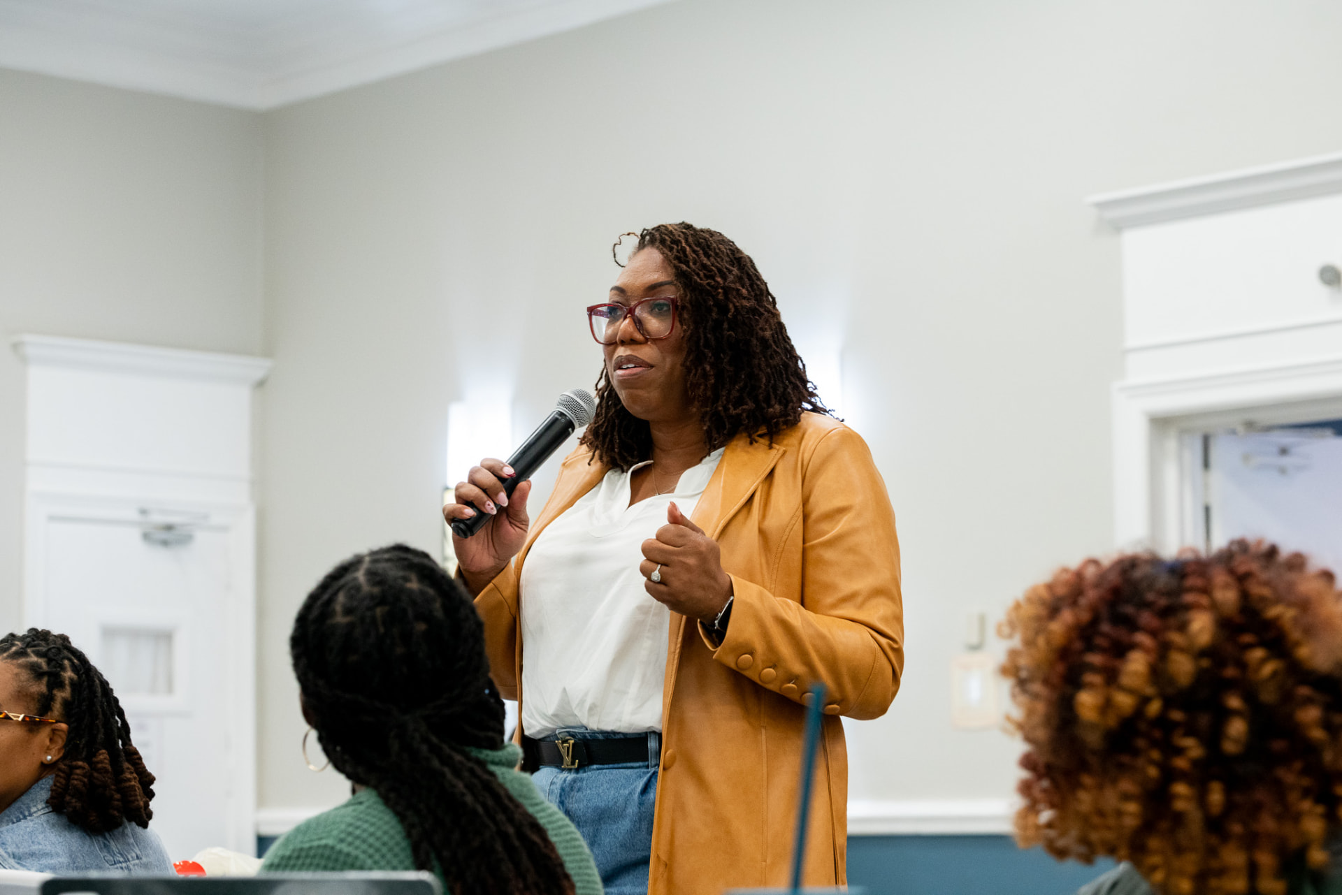 Coach Key in a tan jacket speaking into a microphone among seated workshop attendees