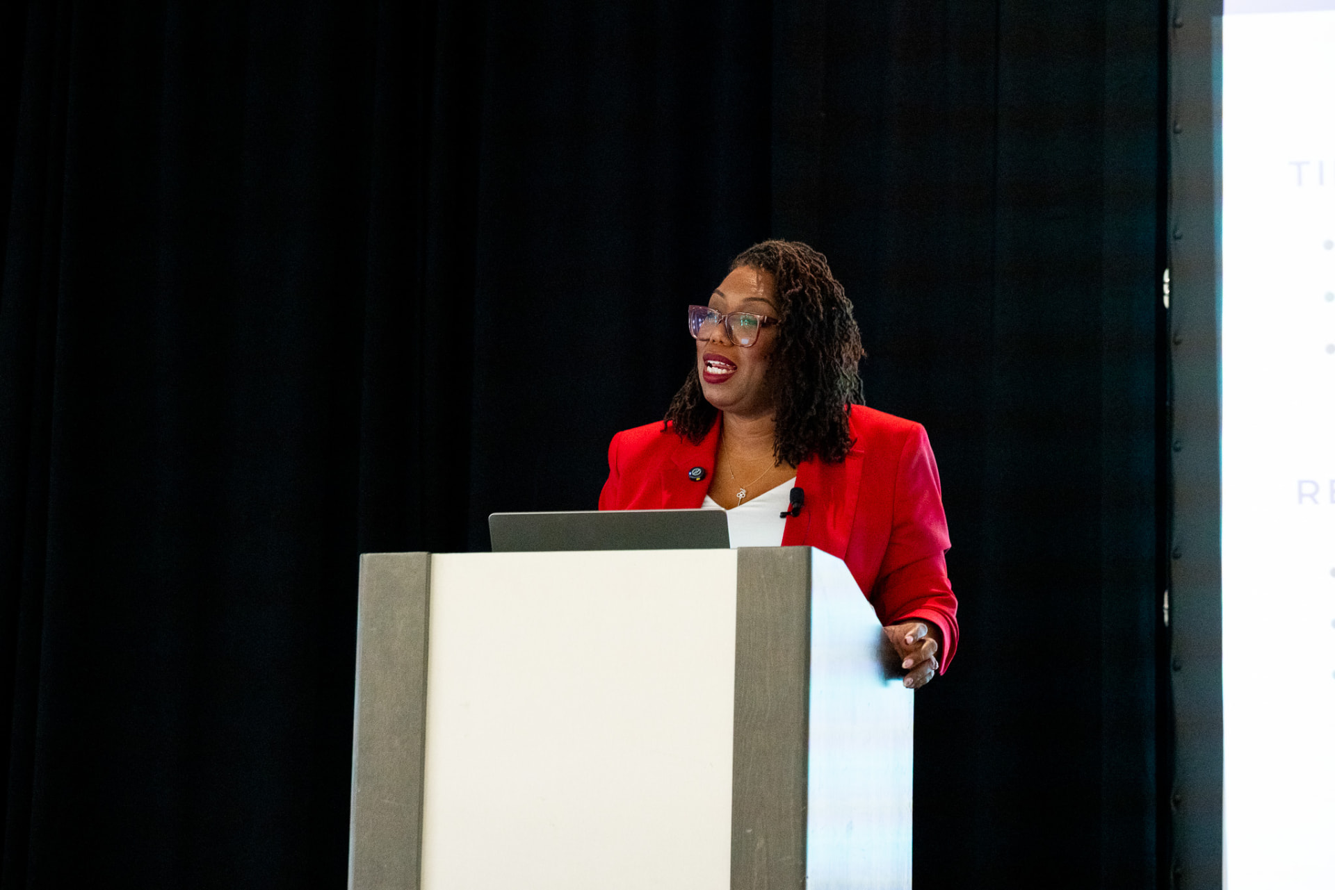 Coach Key at a lectern against a dark curtain during a conference session