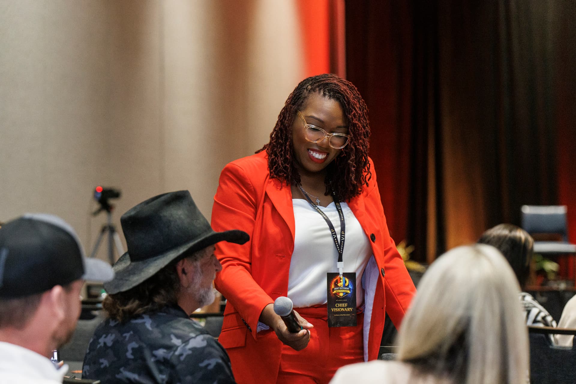 Coach Key smiling as she passes the microphone to an attendee at the Built Different Creator Summit